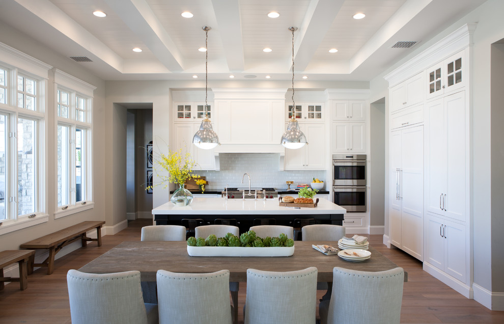 This is an example of a traditional l-shaped eat-in kitchen in Phoenix with a farmhouse sink, shaker cabinets, white cabinets, white splashback, subway tile splashback, stainless steel appliances, medium hardwood floors and with island.