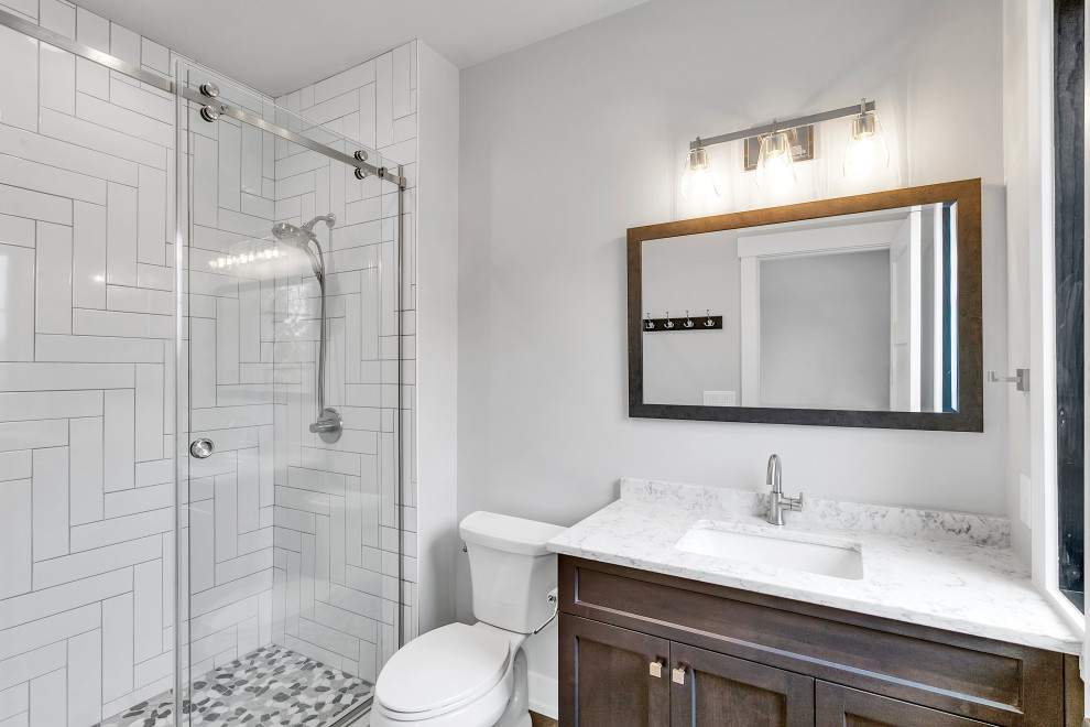 Photo of a large country kids wet room bathroom in Other with shaker cabinets, dark wood cabinets, a two-piece toilet, white tile, white walls, pebble tile floors, an undermount sink, engineered quartz benchtops, grey floor, a sliding shower screen, white benchtops, a single vanity and a built-in vanity.