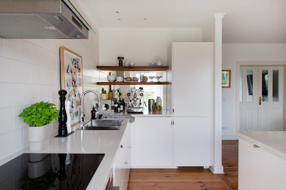 Geräumige Skandinavische Wohnküche in L-Form mit Einbauwaschbecken, flächenbündigen Schrankfronten, weißen Schränken, Quarzwerkstein-Arbeitsplatte, Küchenrückwand in Weiß, Rückwand aus Keramikfliesen, weißen Elektrogeräten, dunklem Holzboden, Kücheninsel, braunem Boden, grauer Arbeitsplatte und eingelassener Decke in Berlin