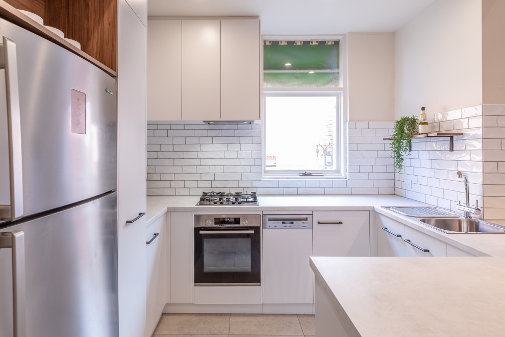 Design ideas for a small contemporary u-shaped kitchen in Adelaide with a double-bowl sink, flat-panel cabinets, white cabinets, laminate benchtops, white splashback, subway tile splashback, stainless steel appliances, cement tiles, a peninsula, grey floor and grey benchtop.