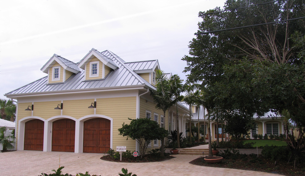 Photo of a large mediterranean two-storey yellow house exterior in Tampa with wood siding, a gable roof and a metal roof.
