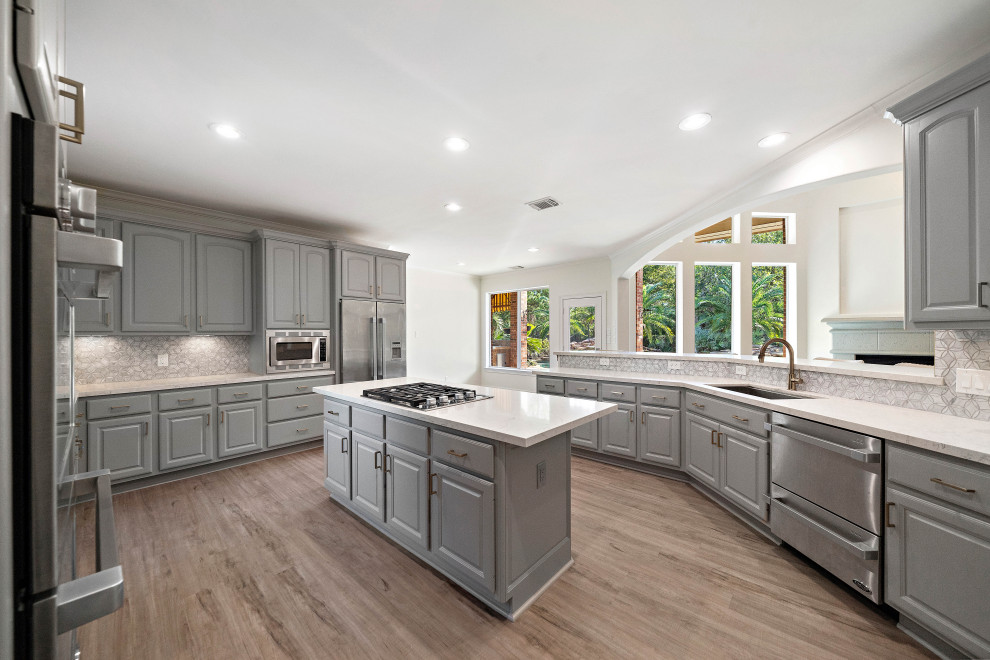 Mid-sized transitional u-shaped light wood floor and brown floor eat-in kitchen photo in Houston with raised-panel cabinets, gray cabinets, white backsplash, marble backsplash, stainless steel appliances, an island, white countertops, quartz countertops and an undermount sink