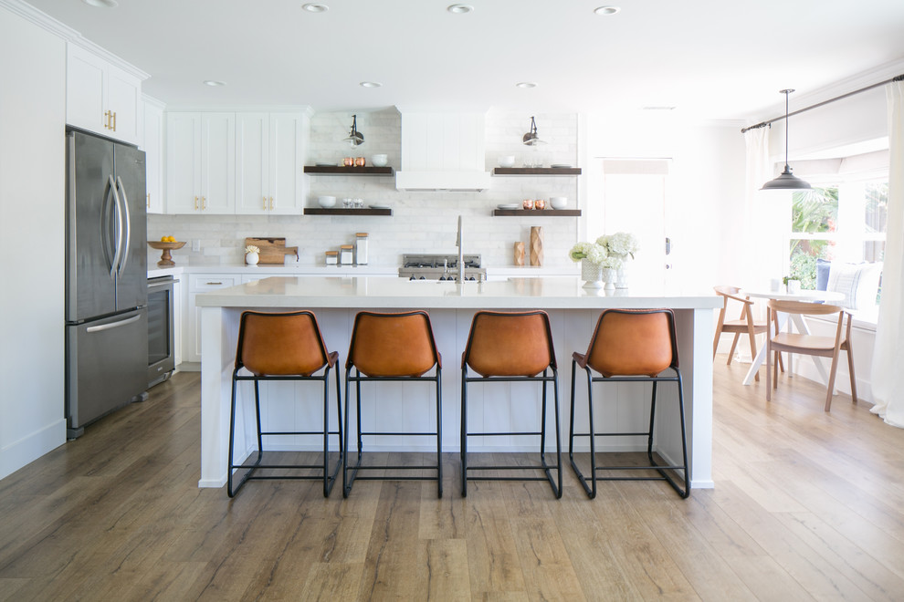 Design ideas for a mid-sized country eat-in kitchen in Orange County with white cabinets, white splashback, medium hardwood floors, with island, subway tile splashback, stainless steel appliances and shaker cabinets.