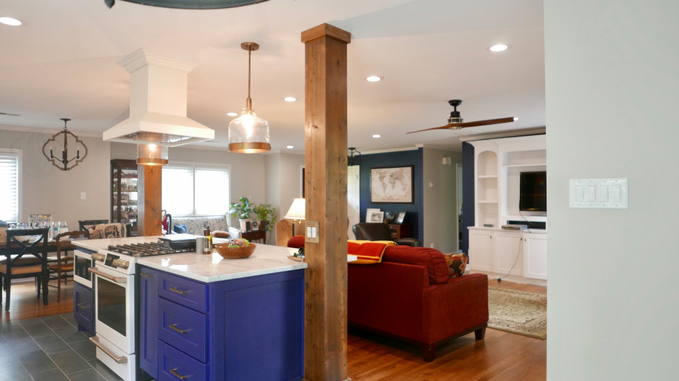 Example of a mid-sized transitional galley porcelain tile and black floor eat-in kitchen design with a farmhouse sink, shaker cabinets, blue cabinets, marble countertops, white backsplash, subway tile backsplash, white appliances, an island and multicolored countertops