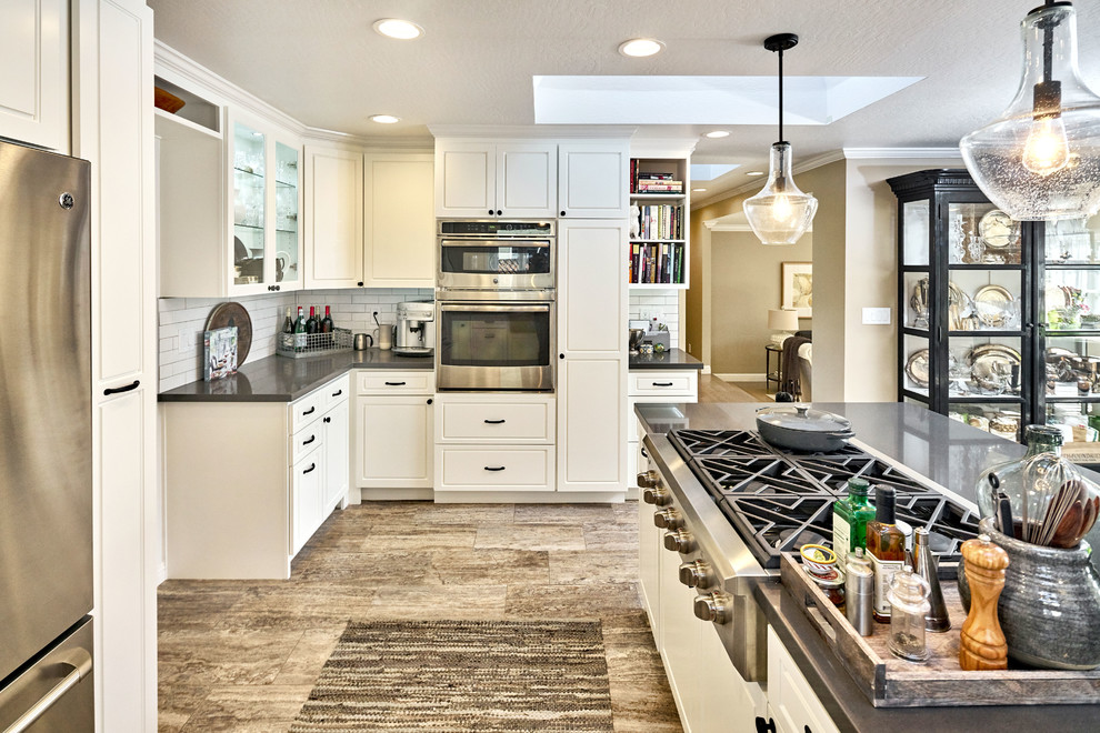 Large country u-shaped open plan kitchen in San Francisco with a farmhouse sink, raised-panel cabinets, white cabinets, soapstone benchtops, white splashback, subway tile splashback, stainless steel appliances, porcelain floors, with island and grey floor.