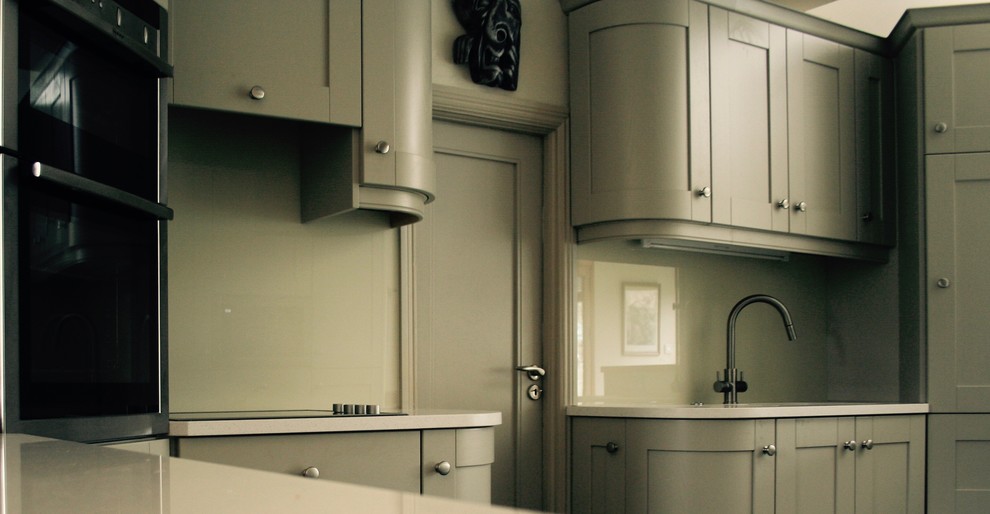 Mid-sized modern u-shaped open plan kitchen in Dublin with an integrated sink, shaker cabinets, grey cabinets, quartzite benchtops, grey splashback, glass sheet splashback, black appliances, ceramic floors and no island.