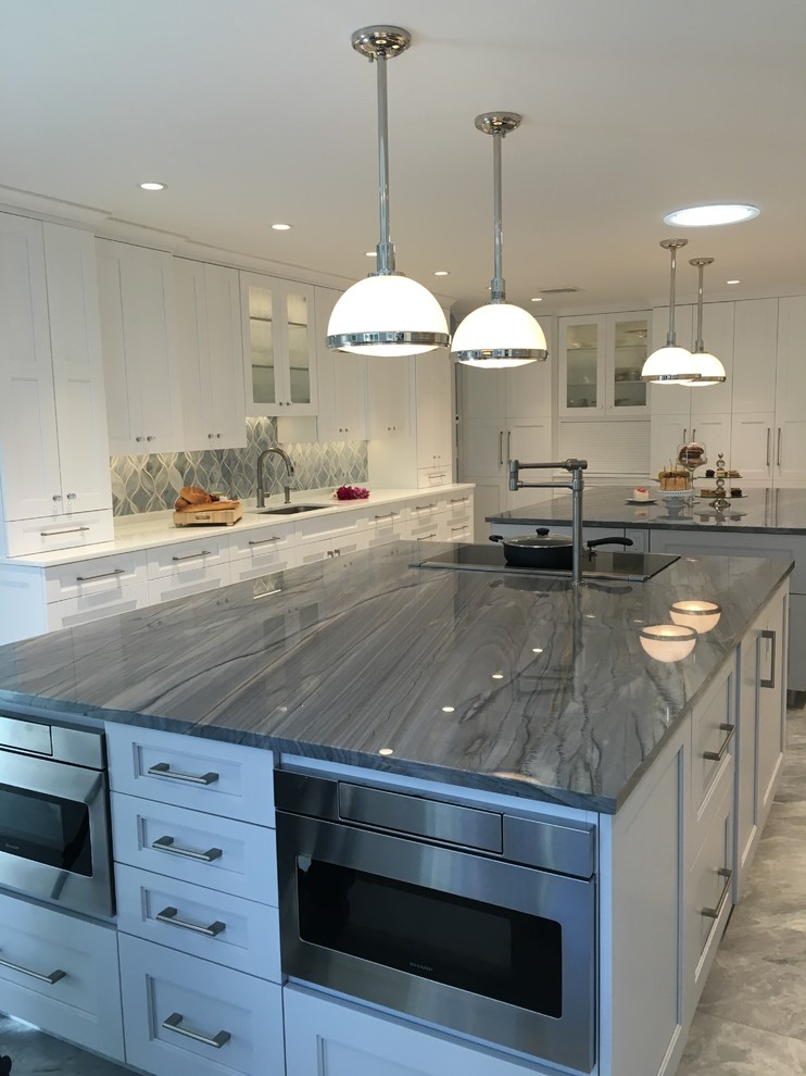 This is an example of an expansive contemporary u-shaped eat-in kitchen in New York with a single-bowl sink, shaker cabinets, white cabinets, quartzite benchtops, grey splashback, glass sheet splashback, stainless steel appliances, ceramic floors and multiple islands.