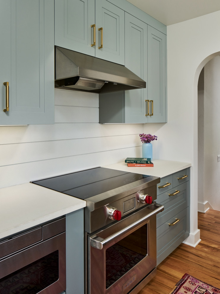 Diseño de cocina clásica renovada pequeña con puertas de armario grises, encimera de cuarzo compacto, electrodomésticos de acero inoxidable, suelo de madera en tonos medios y encimeras blancas