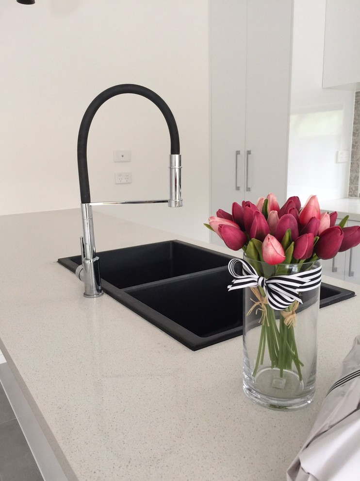 Photo of a mid-sized contemporary galley open plan kitchen in Melbourne with white cabinets, quartz benchtops, glass sheet splashback, stainless steel appliances, porcelain floors and with island.