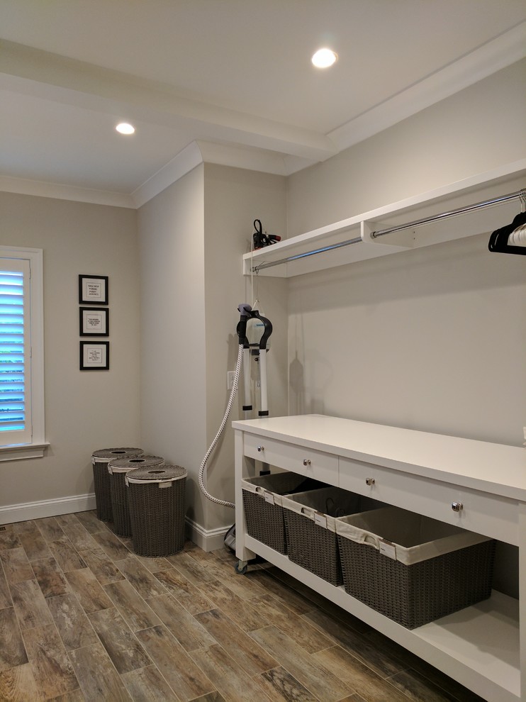 Large transitional dedicated laundry room in Philadelphia with an undermount sink, recessed-panel cabinets, white cabinets, solid surface benchtops, grey walls, a side-by-side washer and dryer, grey floor and light hardwood floors.