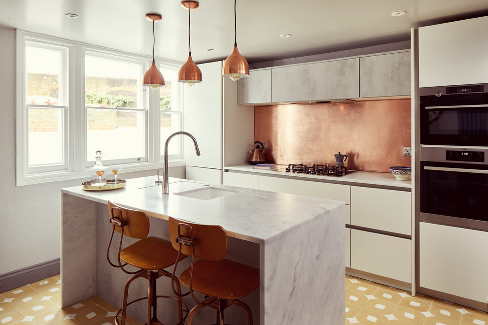 Design ideas for a mid-sized contemporary single-wall open plan kitchen in London with an undermount sink, flat-panel cabinets, white cabinets, marble benchtops, metallic splashback, metal splashback, panelled appliances, ceramic floors, with island, yellow floor and white benchtop.