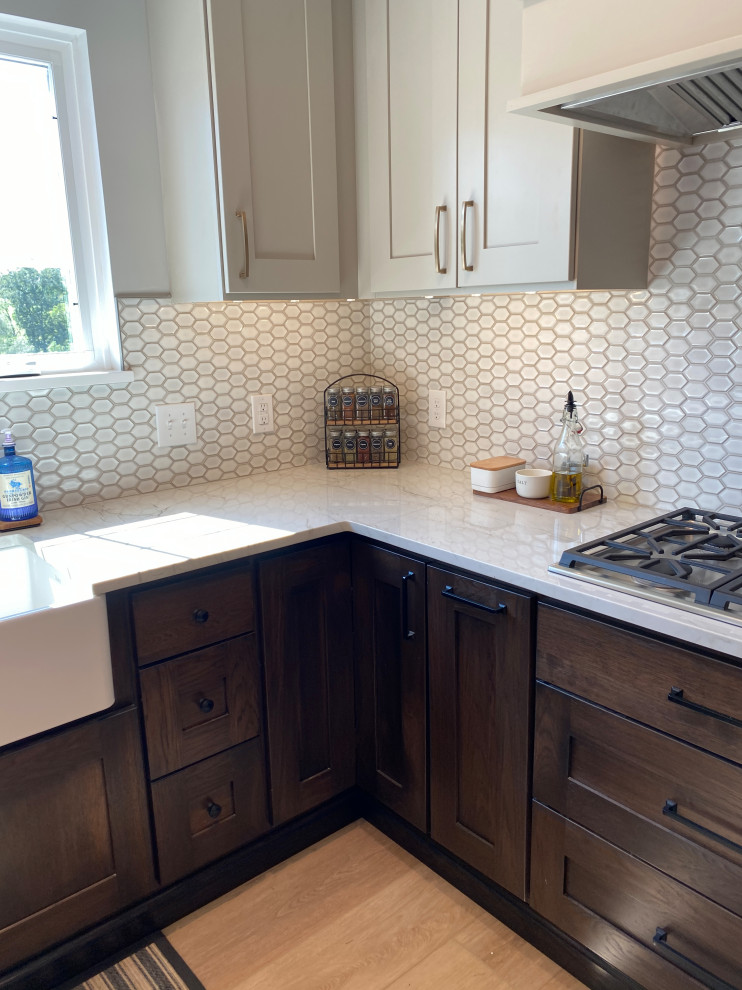 Photo of a mid-sized country u-shaped kitchen pantry in Philadelphia with a farmhouse sink, shaker cabinets, dark wood cabinets, quartzite benchtops, white splashback, mosaic tile splashback, stainless steel appliances, vinyl floors, a peninsula, brown floor and white benchtop.