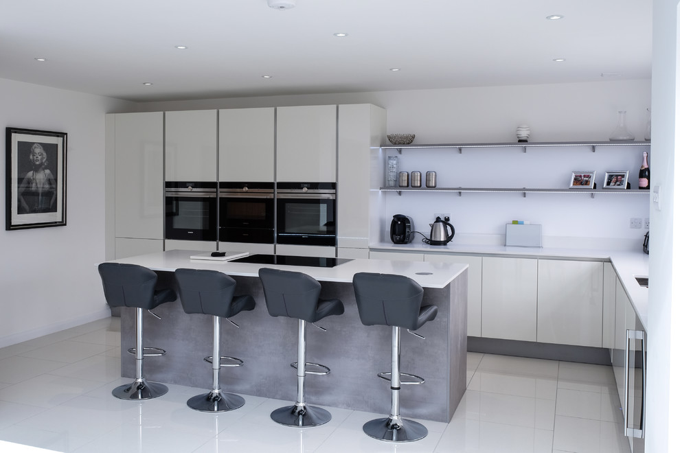 Contemporary l-shaped eat-in kitchen in Essex with an undermount sink, flat-panel cabinets, beige cabinets, quartzite benchtops, beige splashback, stone slab splashback, black appliances, porcelain floors and with island.