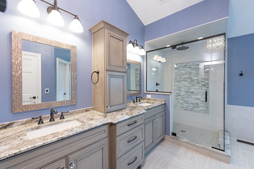 This is an example of a mid-sized traditional master bathroom in Indianapolis with beaded inset cabinets, grey cabinets, a corner shower, white tile, glass sheet wall, blue walls, ceramic floors, an undermount sink, granite benchtops, a hinged shower door, multi-coloured benchtops, a double vanity and a built-in vanity.