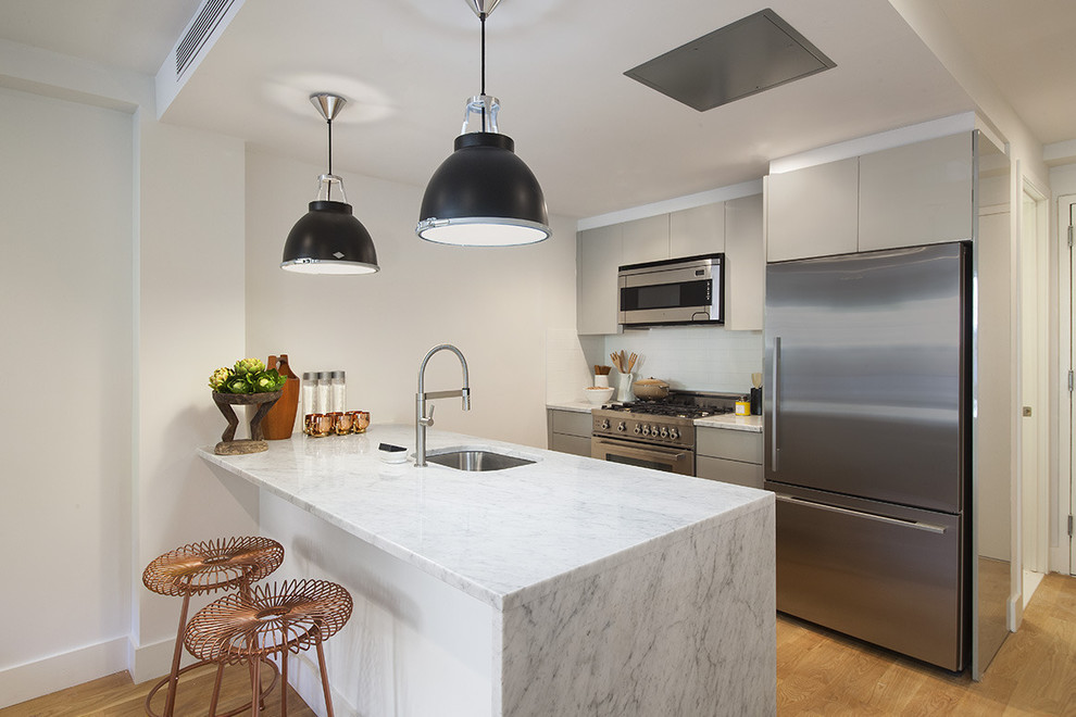 Contemporary galley kitchen in New York with an undermount sink, flat-panel cabinets, grey cabinets, stainless steel appliances, light hardwood floors and a peninsula.
