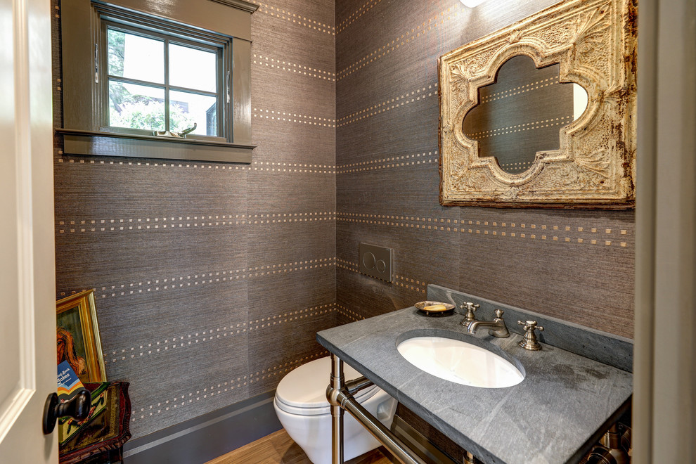 This is an example of a small transitional powder room in San Francisco with a wall-mount toilet, brown walls, light hardwood floors, a drop-in sink, soapstone benchtops, brown floor and black benchtops.