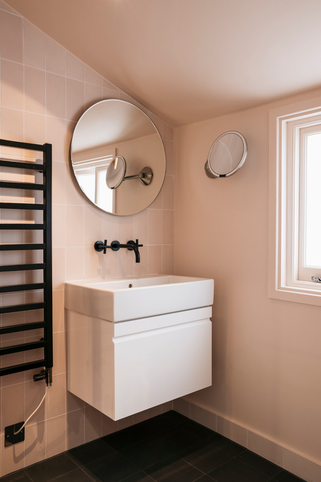 Design ideas for a mid-sized contemporary bathroom in London with flat-panel cabinets, white cabinets, porcelain tile, porcelain floors, black floor, pink tile, pink walls and a console sink.