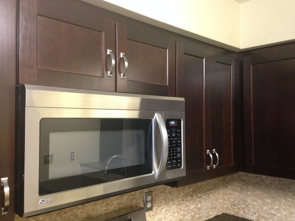 Example of a mid-sized transitional l-shaped porcelain tile enclosed kitchen design with an undermount sink, shaker cabinets, dark wood cabinets, granite countertops, beige backsplash, stone tile backsplash, stainless steel appliances and an island
