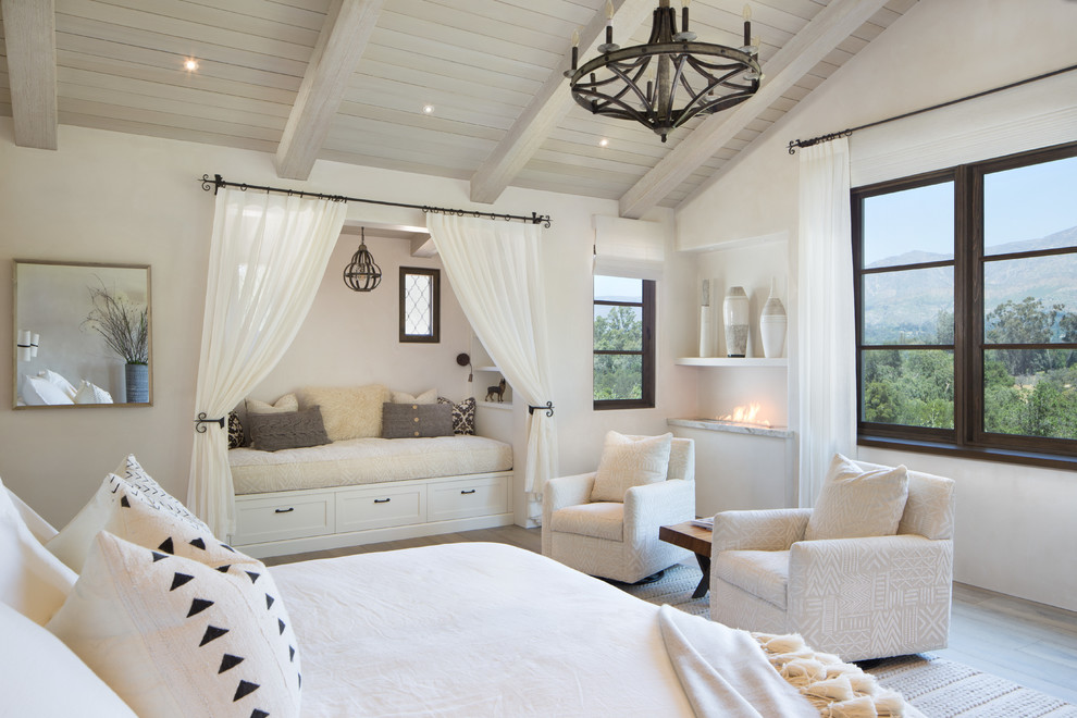 Design ideas for a large mediterranean master bedroom in Santa Barbara with white walls, light hardwood floors, a ribbon fireplace and brown floor.