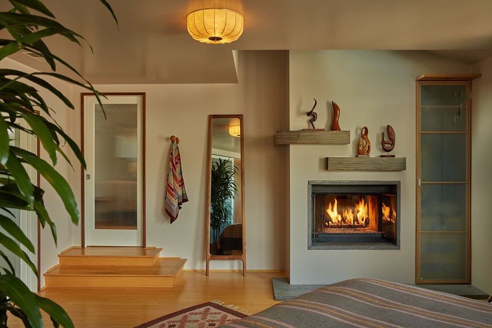 Midcentury master bedroom in Los Angeles with bamboo floors, a two-sided fireplace and a concrete fireplace surround.