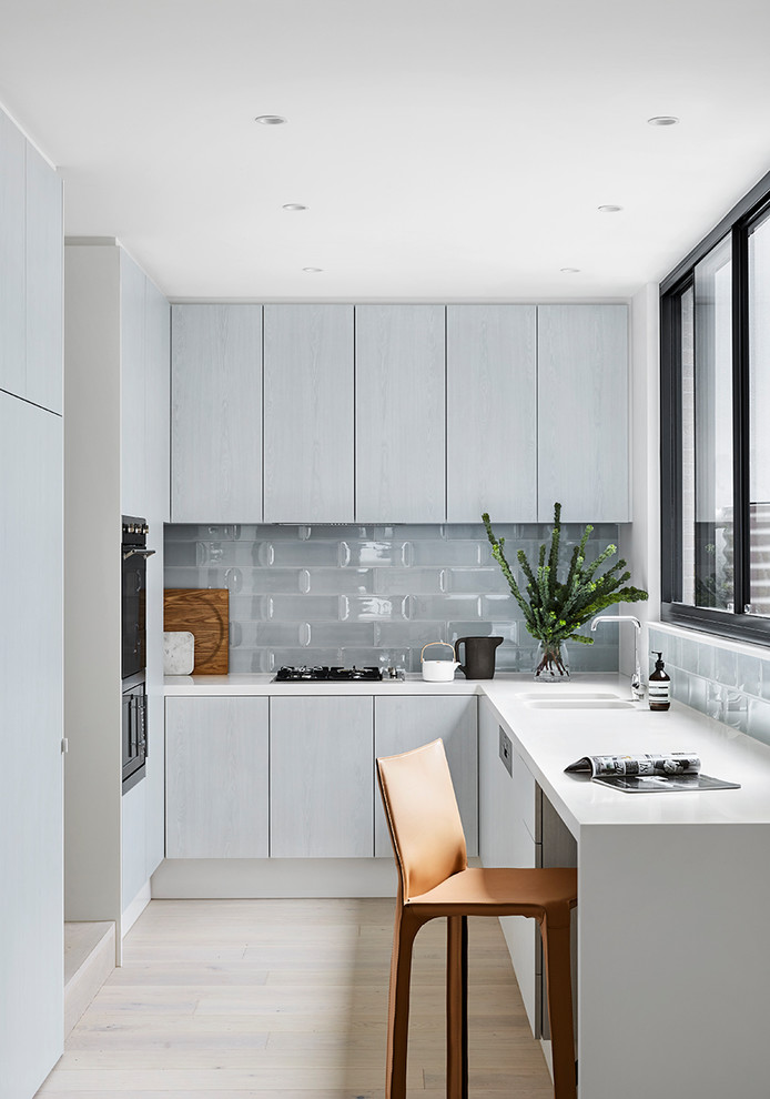 Contemporary kitchen in Melbourne with an undermount sink, grey splashback, ceramic splashback, white benchtop, quartz benchtops, black appliances and light hardwood floors.