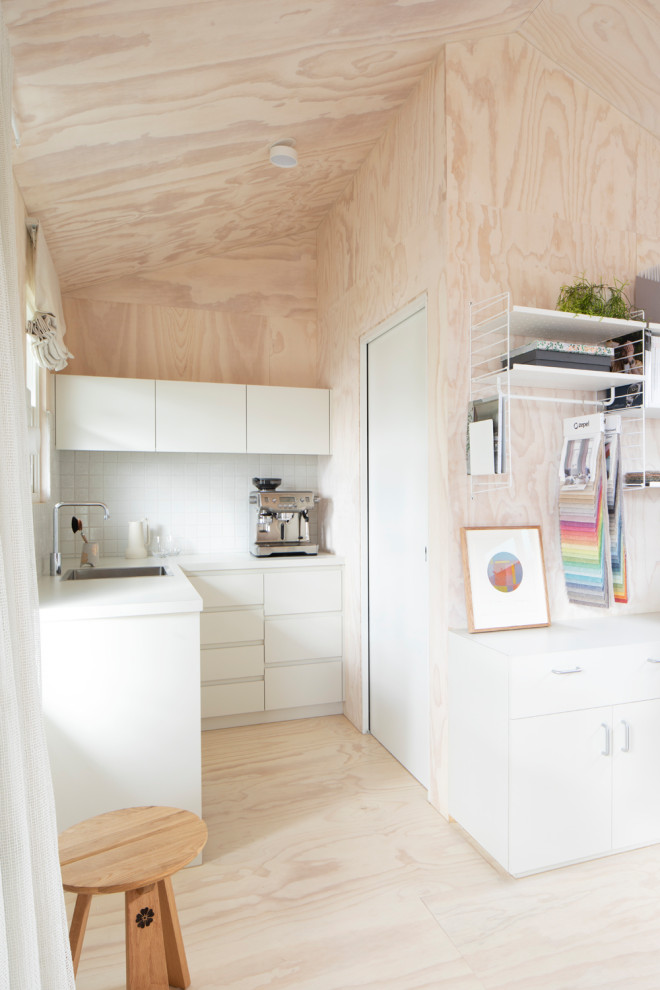 Foto på ett litet funkis vit kök, med en integrerad diskho, släta luckor, vita skåp, laminatbänkskiva, vitt stänkskydd, stänkskydd i mosaik, rostfria vitvaror, målat trägolv och vitt golv
