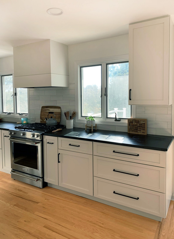 Design ideas for a large contemporary open plan kitchen in Philadelphia with a submerged sink, shaker cabinets, grey cabinets, soapstone worktops, grey splashback, ceramic splashback, stainless steel appliances, light hardwood flooring, an island, brown floors and black worktops.