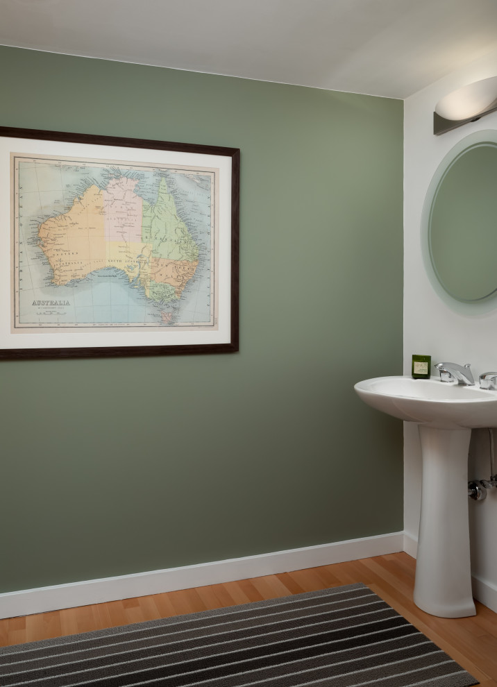 Modelo de cuarto de baño único, de pie, blanco y blanco y madera actual pequeño con sanitario de una pieza, paredes verdes, suelo de madera en tonos medios, aseo y ducha, lavabo con pedestal y suelo naranja