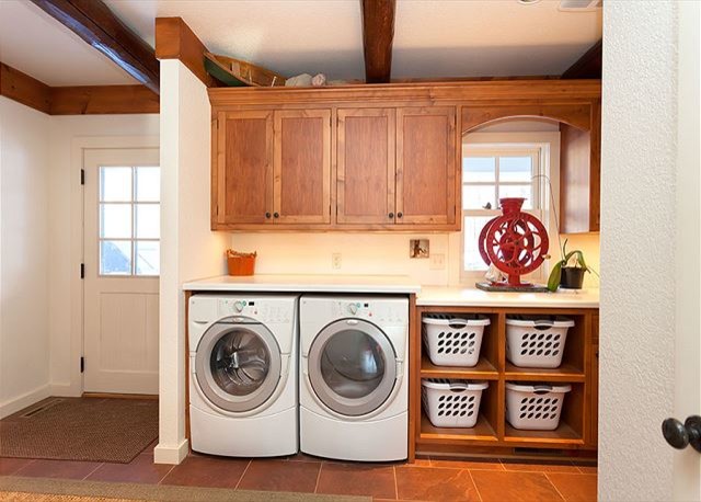 Inspiration for a mid-sized rustic single-wall ceramic tile and brown floor dedicated laundry room remodel with medium tone wood cabinets, solid surface countertops, white walls, a side-by-side washer/dryer and recessed-panel cabinets