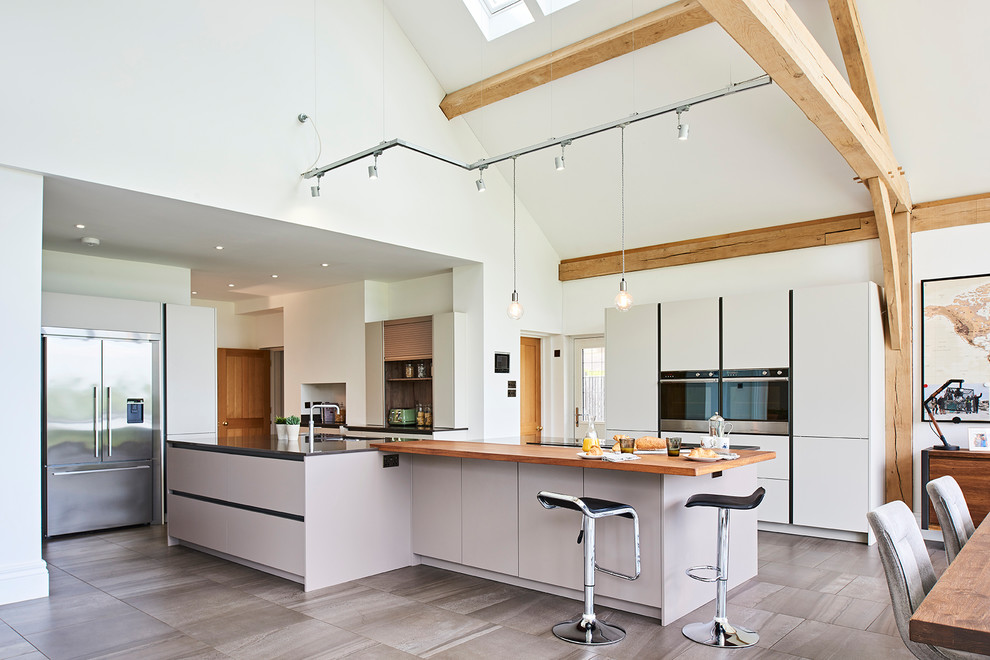 Expansive contemporary open plan kitchen in Hertfordshire with flat-panel cabinets, quartzite benchtops, panelled appliances, porcelain floors, grey floor, grey benchtop, white cabinets and with island.