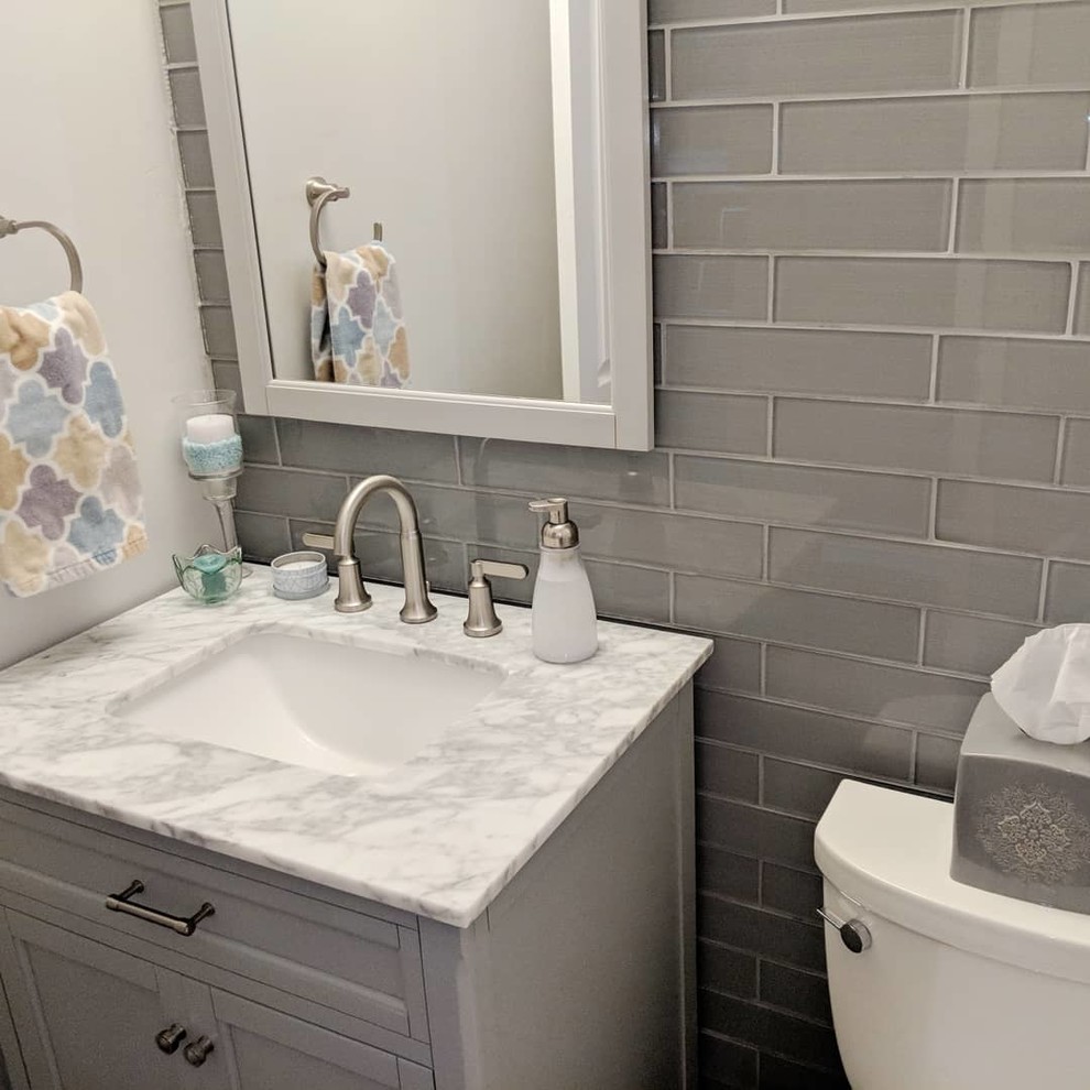 This is an example of a small contemporary powder room in Indianapolis with flat-panel cabinets, grey cabinets, a two-piece toilet, blue tile, glass tile, grey walls, laminate floors, an undermount sink, marble benchtops, grey floor and white benchtops.