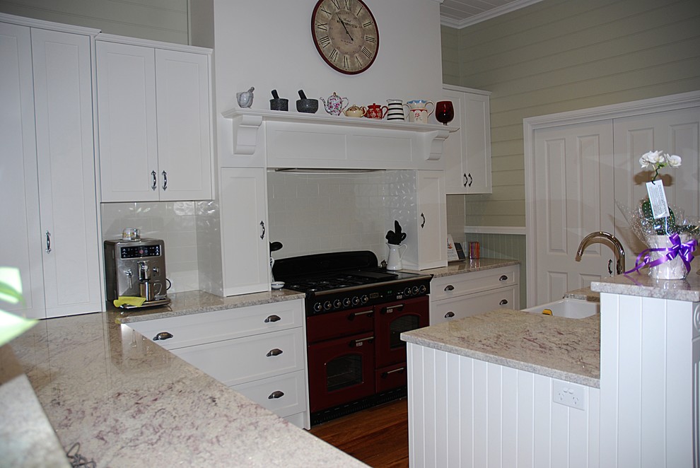 Photo of a large traditional l-shaped eat-in kitchen in Sydney with a farmhouse sink, shaker cabinets, white cabinets, granite benchtops, white splashback, ceramic splashback, coloured appliances, medium hardwood floors and with island.