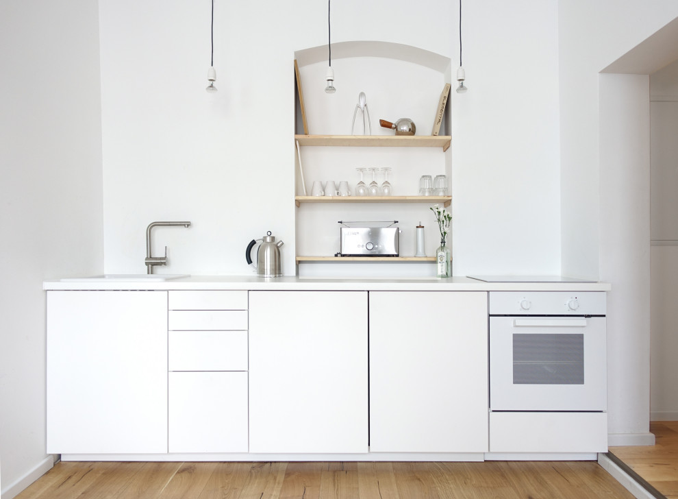 Inredning av ett modernt litet vit linjärt vitt kök och matrum, med en integrerad diskho, släta luckor, vita skåp, laminatbänkskiva, vitt stänkskydd, vita vitvaror, ljust trägolv och beiget golv