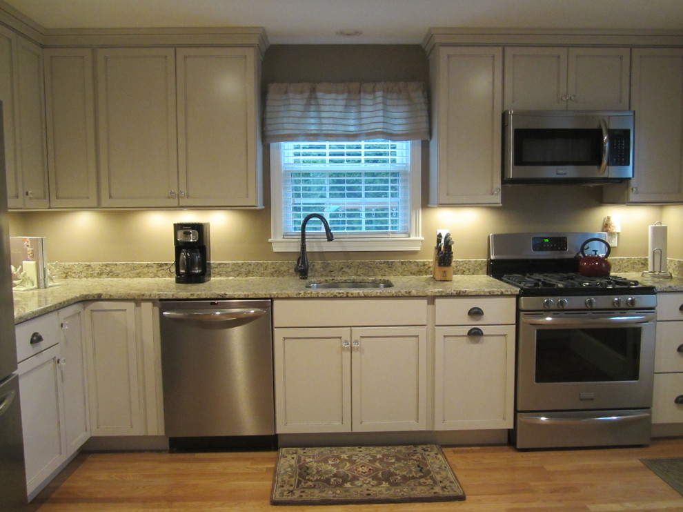 This is an example of a mid-sized transitional l-shaped eat-in kitchen in Providence with an undermount sink, shaker cabinets, white cabinets, granite benchtops, stainless steel appliances, beige splashback, medium hardwood floors and a peninsula.