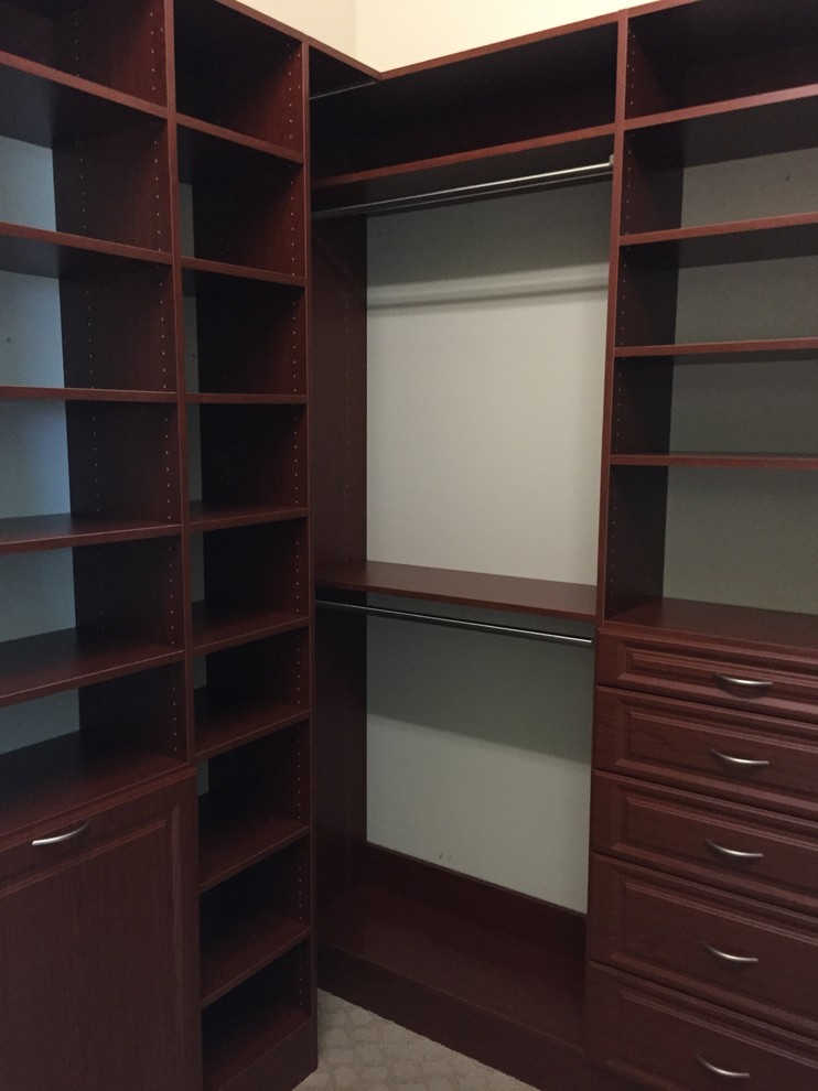 Photo of a mid-sized traditional gender-neutral walk-in wardrobe in Miami with open cabinets, dark wood cabinets and carpet.