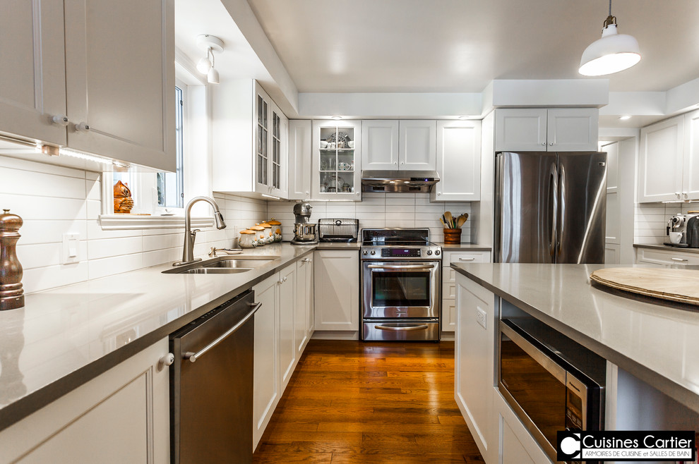 Large transitional medium tone wood floor eat-in kitchen photo in Montreal with a double-bowl sink, shaker cabinets, white cabinets, quartzite countertops, white backsplash, ceramic backsplash, stainless steel appliances and an island