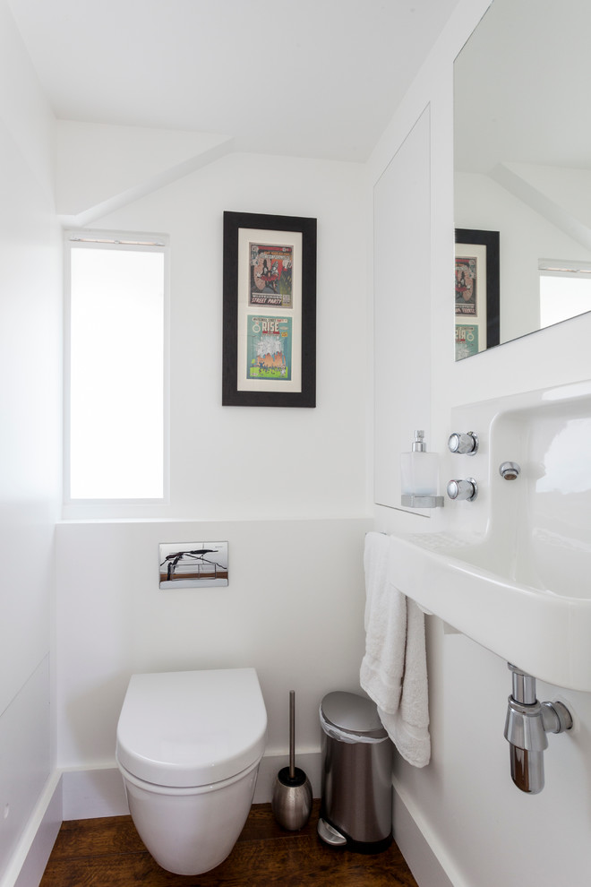 This is an example of a small contemporary powder room in London with a wall-mount sink, white walls and dark hardwood floors.