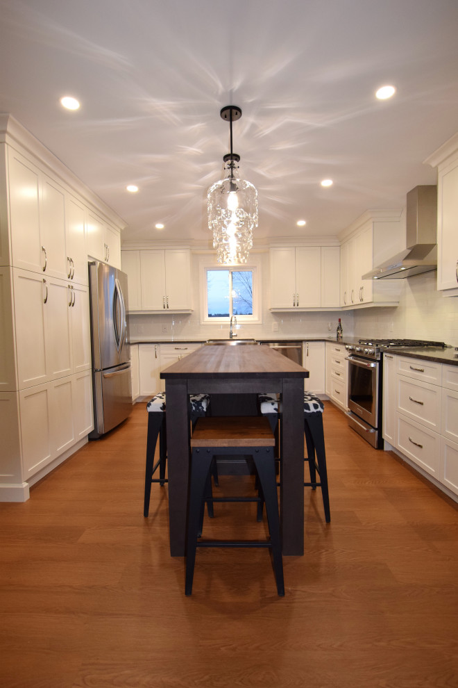 Small transitional u-shaped medium tone wood floor and brown floor open concept kitchen photo in Ottawa with a farmhouse sink, shaker cabinets, white cabinets, quartz countertops, white backsplash, subway tile backsplash, stainless steel appliances, an island and gray countertops