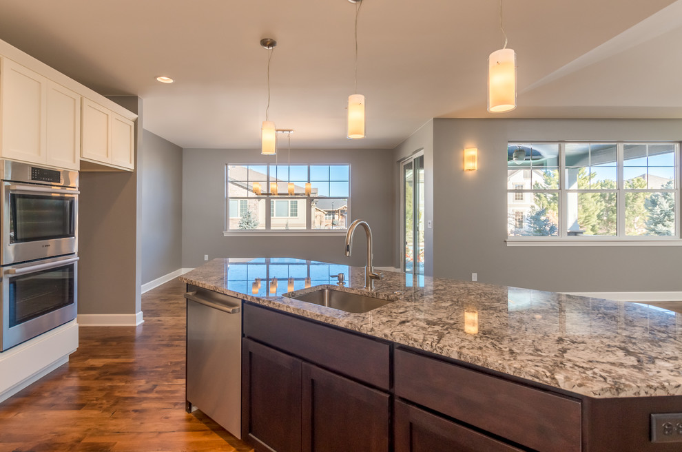 Open concept kitchen - transitional l-shaped medium tone wood floor open concept kitchen idea in Denver with recessed-panel cabinets, dark wood cabinets, granite countertops, an island, an undermount sink, beige backsplash, stone tile backsplash and stainless steel appliances