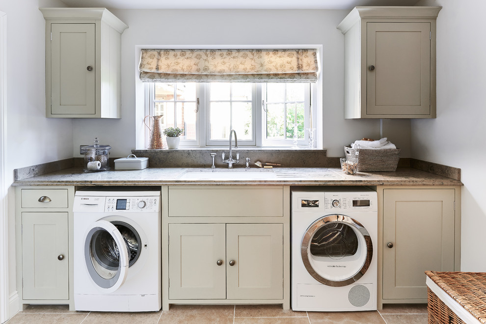 Design ideas for a mid-sized traditional single-wall laundry room in Berkshire with a drop-in sink, shaker cabinets, white cabinets, limestone benchtops, white walls, limestone floors and a side-by-side washer and dryer.