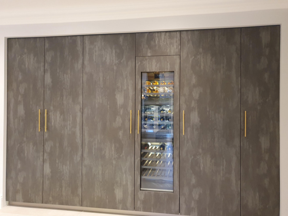 Large contemporary single-wall eat-in kitchen in London with a drop-in sink, flat-panel cabinets, grey cabinets, solid surface benchtops, grey splashback, mirror splashback, black appliances, ceramic floors, with island, white floor and multi-coloured benchtop.