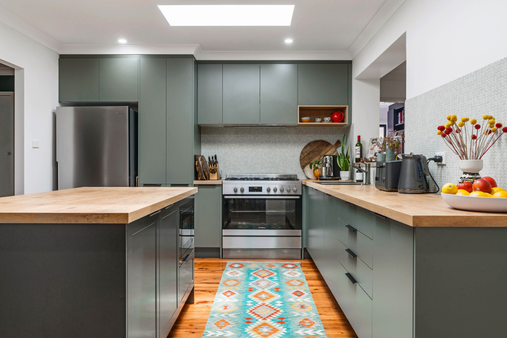 This is an example of a mid-sized contemporary l-shaped kitchen in Sydney with a drop-in sink, flat-panel cabinets, green cabinets, wood benchtops, grey splashback, stainless steel appliances, with island, brown benchtop, mosaic tile splashback, medium hardwood floors and brown floor.