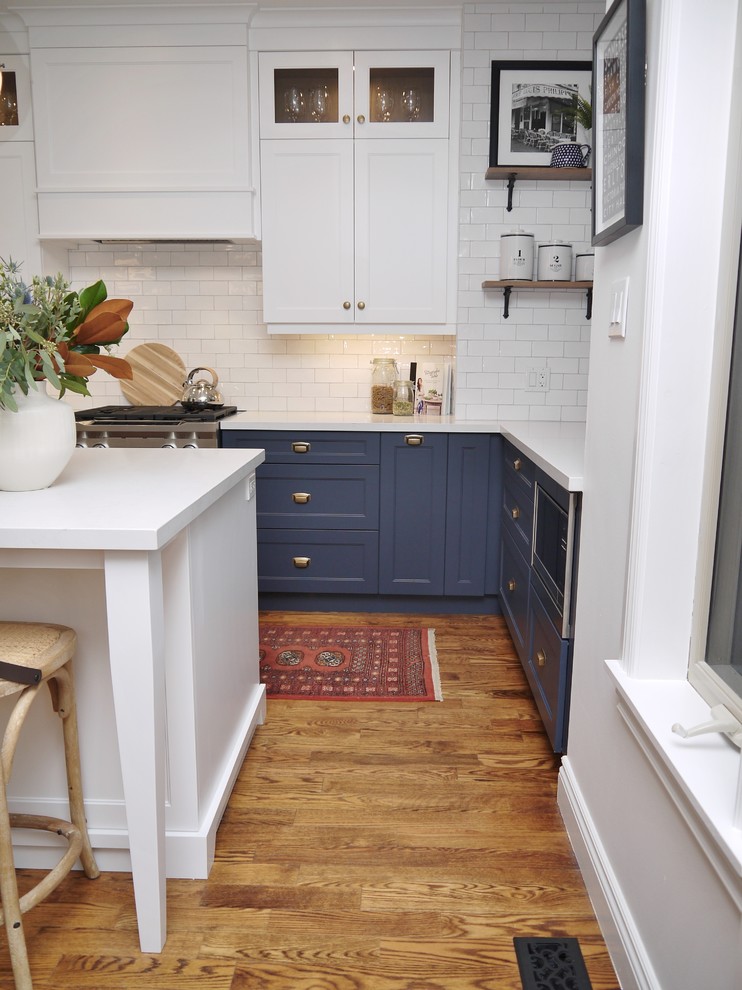 Inspiration for a mid-sized transitional l-shaped medium tone wood floor and brown floor eat-in kitchen remodel in Toronto with an undermount sink, shaker cabinets, blue cabinets, quartz countertops, white backsplash, subway tile backsplash, stainless steel appliances, an island and white countertops
