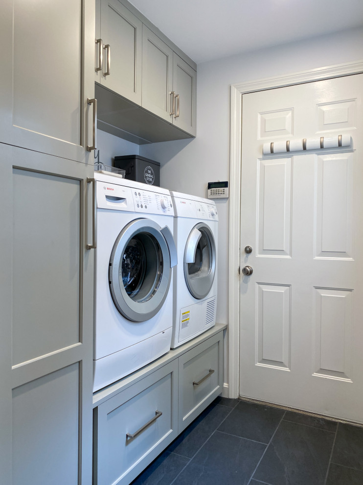 Exempel på en klassisk linjär tvättstuga, med grå skåp, grå väggar, klinkergolv i porslin, en tvättmaskin och torktumlare bredvid varandra och svart golv