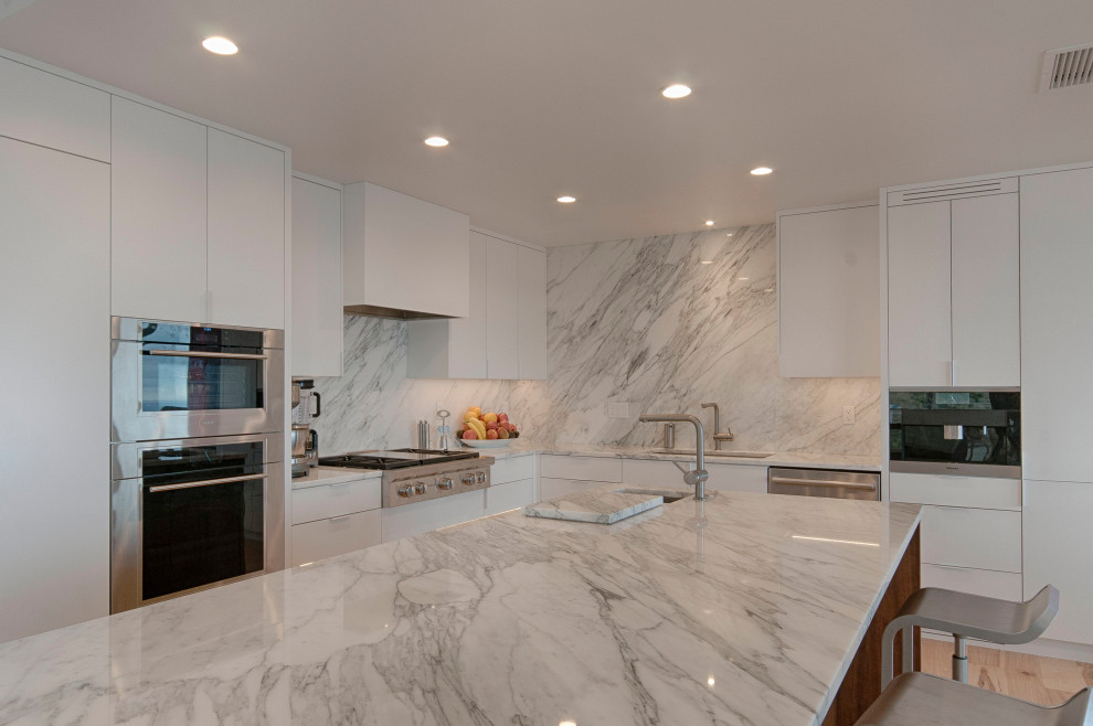 Design ideas for a large contemporary l-shaped eat-in kitchen in Denver with an undermount sink, flat-panel cabinets, white cabinets, marble benchtops, white splashback, marble splashback, stainless steel appliances, light hardwood floors, with island, beige floor, white benchtop and vaulted.