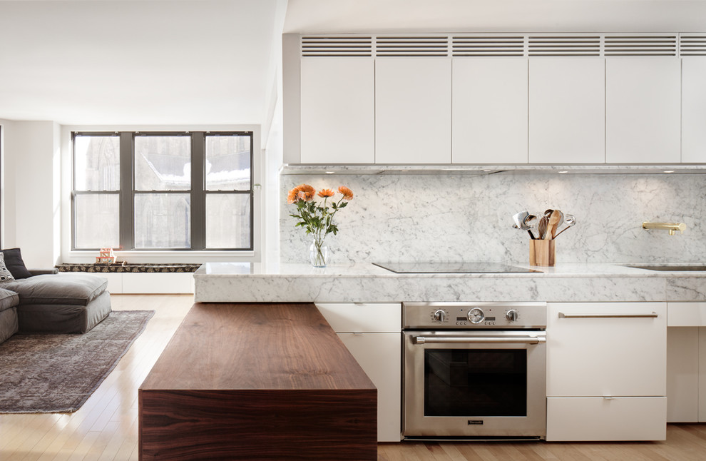 Photo of a mid-sized contemporary l-shaped eat-in kitchen in Boston with an undermount sink, flat-panel cabinets, white cabinets, marble benchtops, light hardwood floors, a peninsula, white splashback, stone slab splashback and stainless steel appliances.