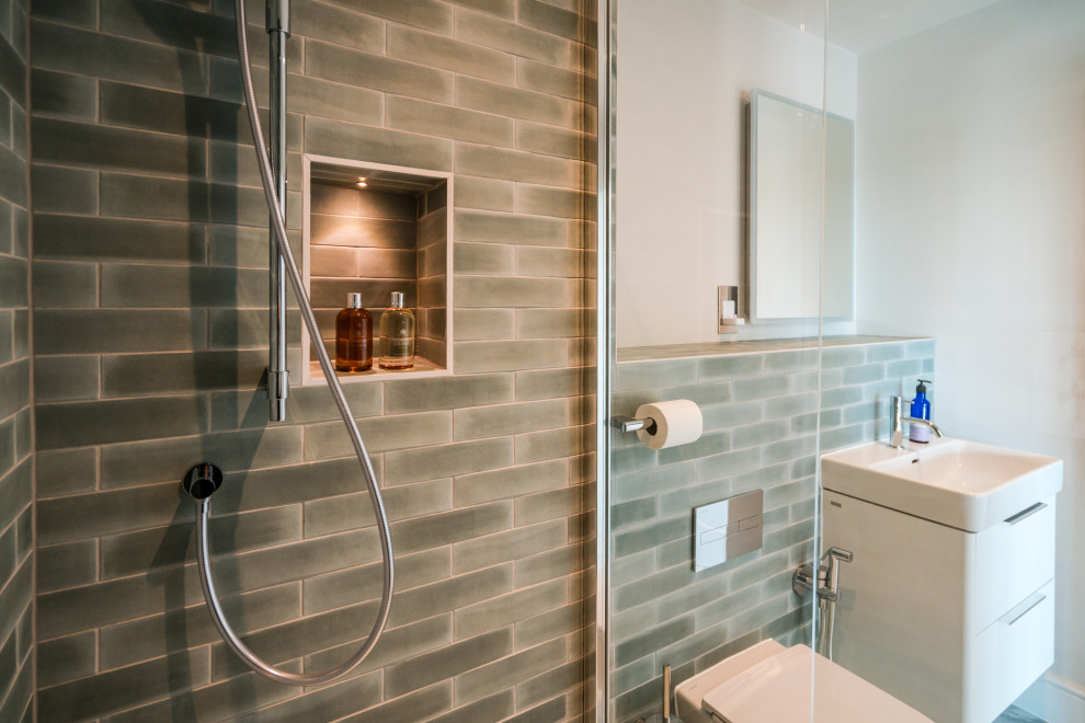 Small beach style grey and teal ensuite bathroom in Hampshire with glass-front cabinets, grey cabinets, a built-in shower, a wall mounted toilet, grey walls, ceramic flooring, a wall-mounted sink, a wall niche, a single sink and a floating vanity unit.