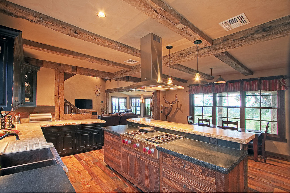 Eat-in kitchen - mid-sized rustic u-shaped medium tone wood floor and brown floor eat-in kitchen idea in Austin with a farmhouse sink, raised-panel cabinets, black cabinets, quartz countertops, stainless steel appliances and an island