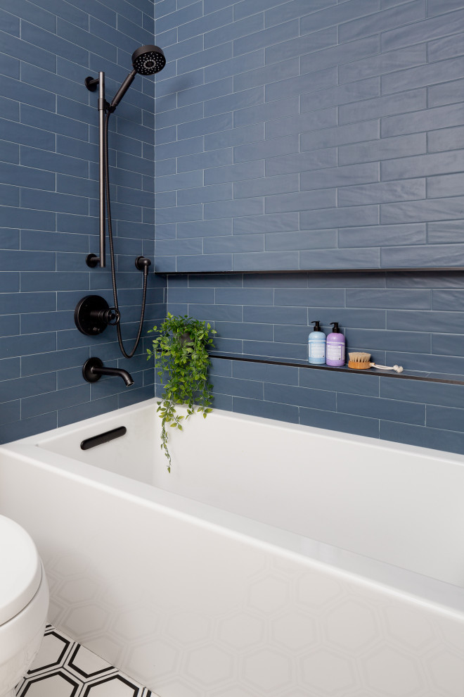 Modern inredning av ett litet badrum med dusch, med skåp i mellenmörkt trä, ett badkar i en alkov, en toalettstol med hel cisternkåpa, blå kakel, porslinskakel, vita väggar, klinkergolv i porslin och vitt golv