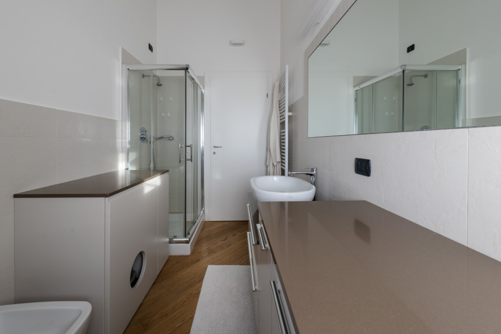 This is an example of a mid-sized scandinavian 3/4 bathroom in Milan with flat-panel cabinets, beige cabinets, a corner shower, a two-piece toilet, white tile, ceramic tile, white walls, light hardwood floors, a vessel sink, engineered quartz benchtops, beige floor, a sliding shower screen, beige benchtops, a single vanity, a built-in vanity and exposed beam.